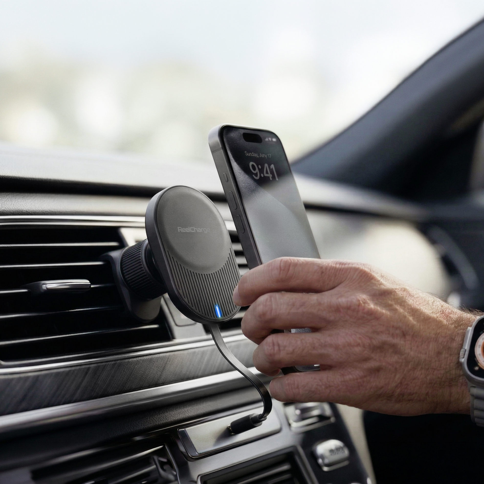 Driver placing an iPhone on the ReelCharge magnetic vent mount charger clipped to a car air vent