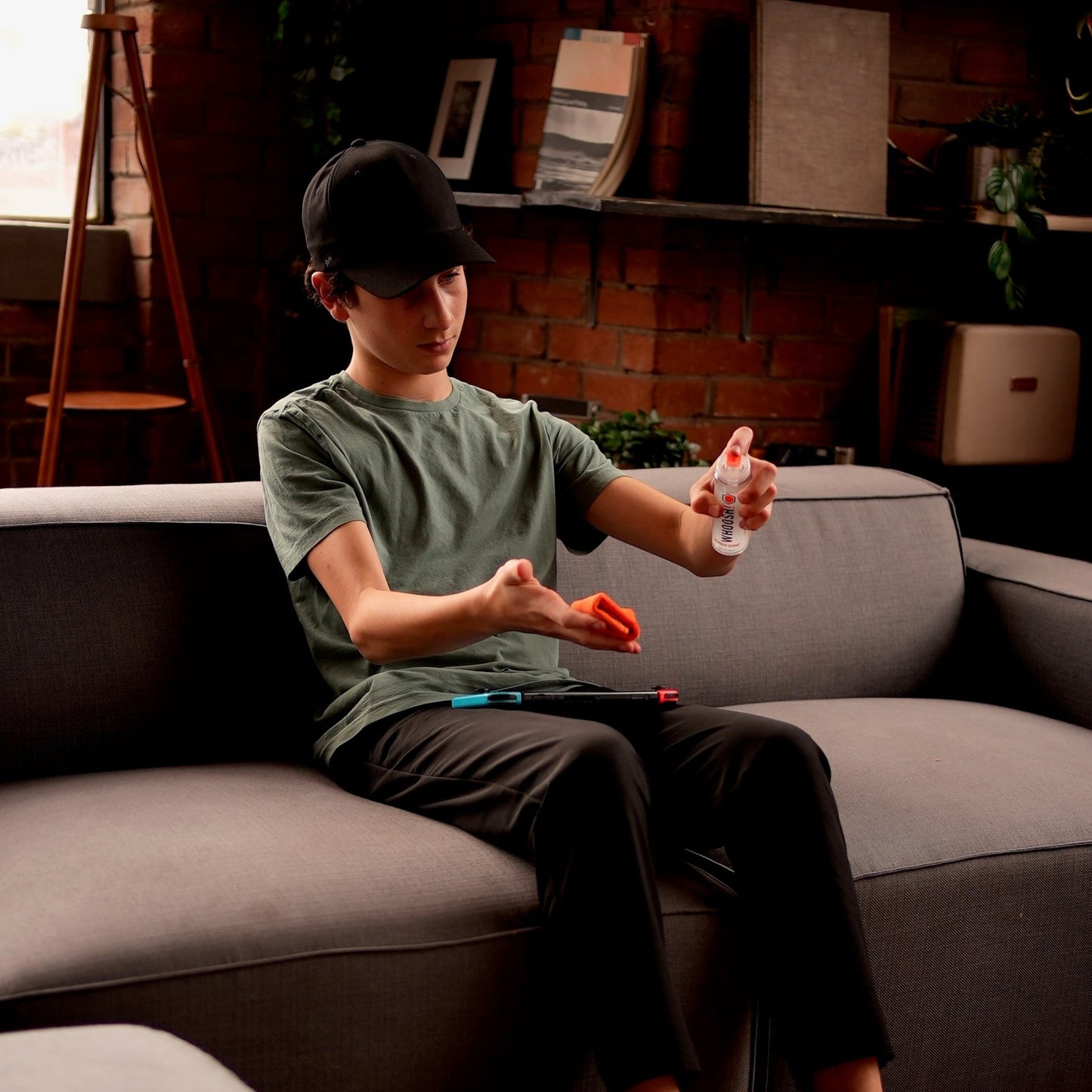 Teen on a couch spraying Whoosh Screen Shine onto a cloth to clean a game controller