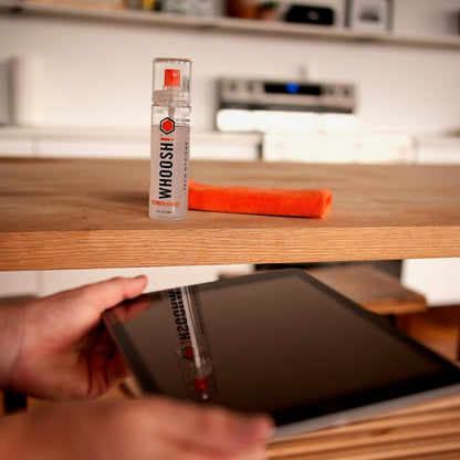 Whoosh Go XL bottle on a table and hands wiping a tablet screen with the orange cloth
