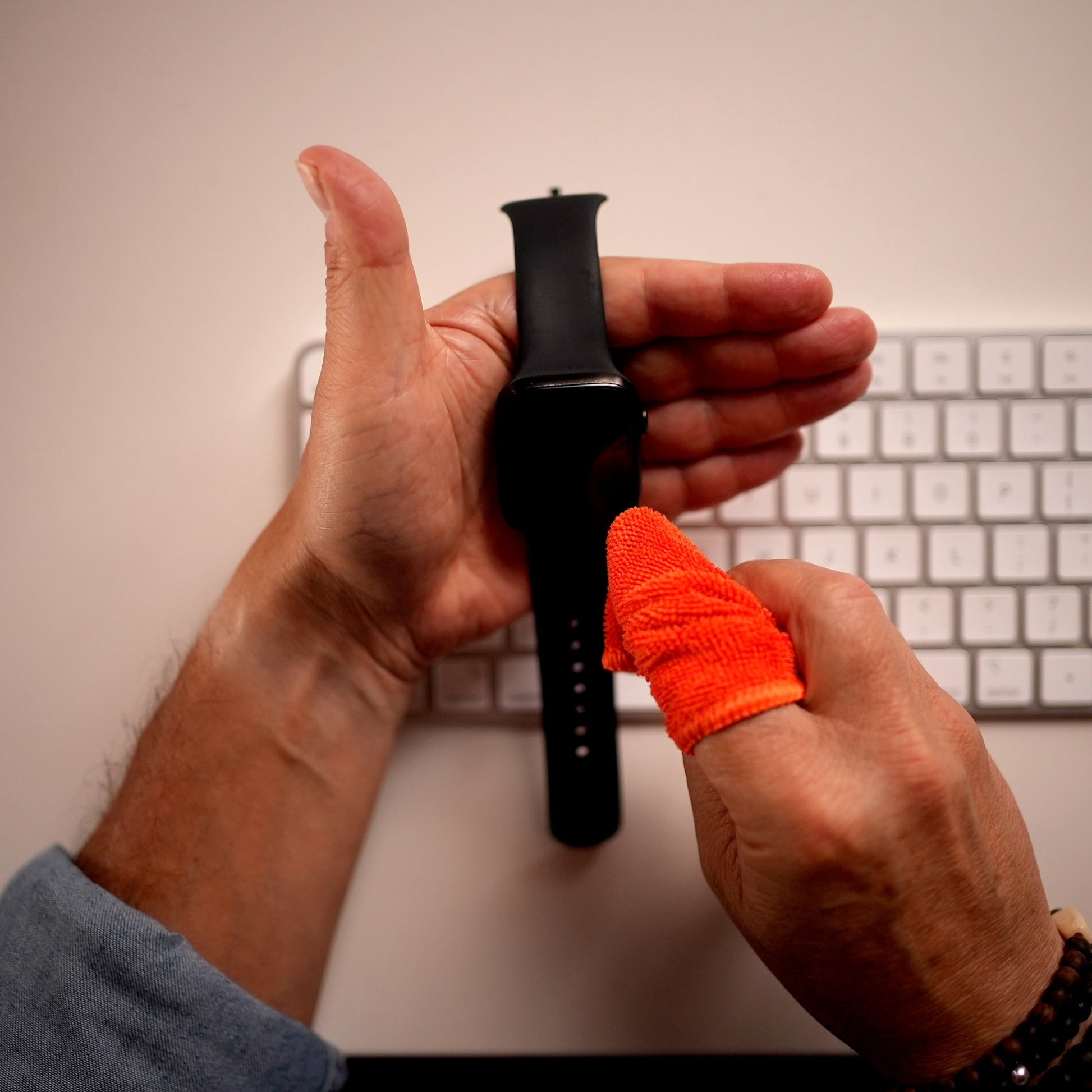 Cleaning a smartwatch band with the orange Whoosh microfiber cloth over a keyboard