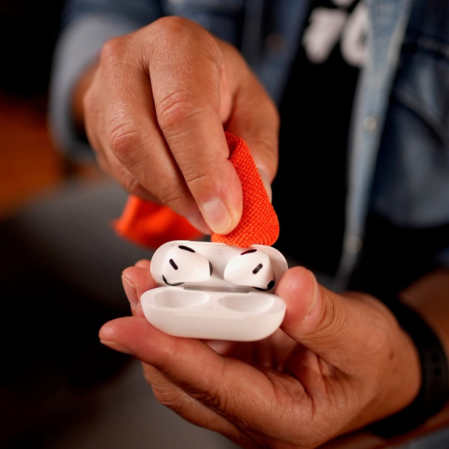 Cleaning wireless earbuds and case with the orange Whoosh microfiber cloth