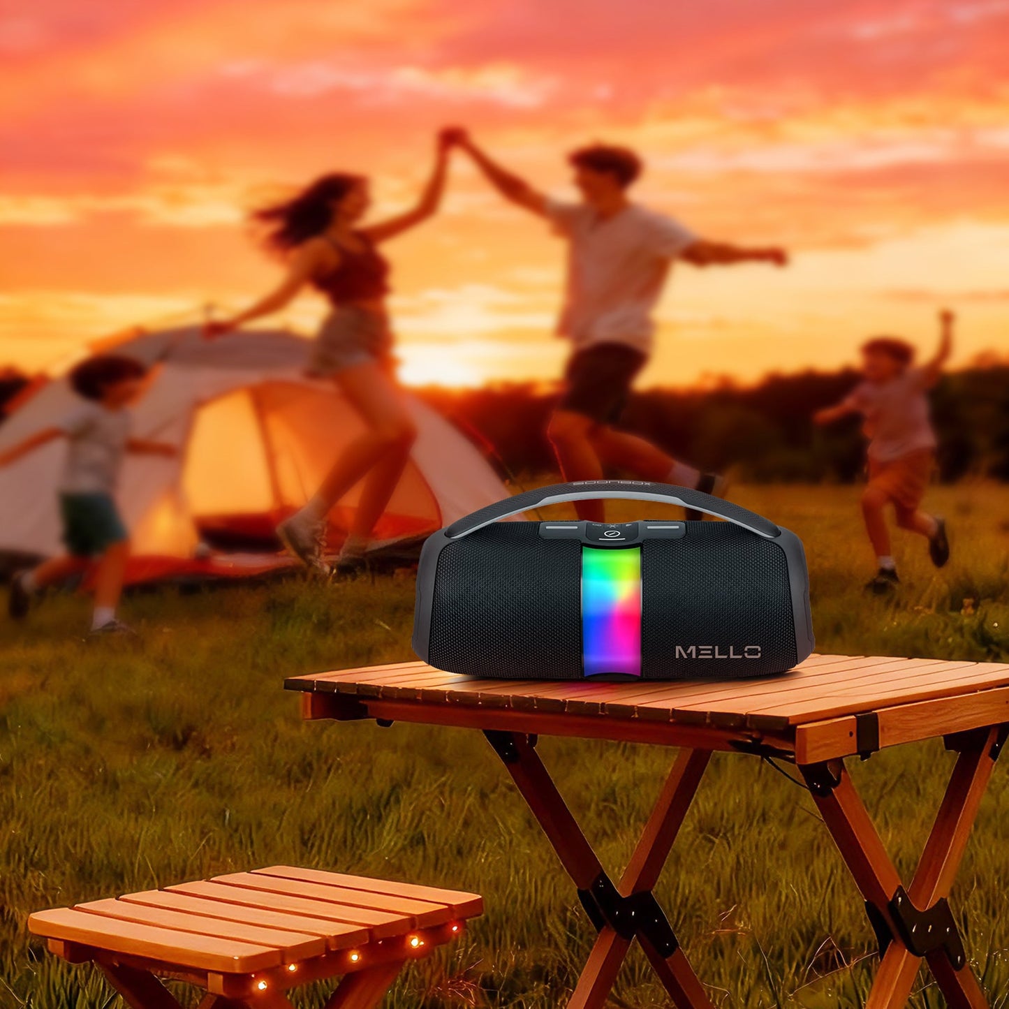 Mello Nomix speaker with RGB lights on a camp table while a family dances at sunset