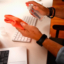 Wiping a Mac keyboard with the orange Whoosh microfiber cloth while holding the Go XL bottle