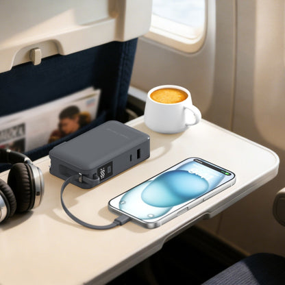 Gray ReelCharge Flex 65W power bank charging a phone on an airplane tray table beside a coffee cup